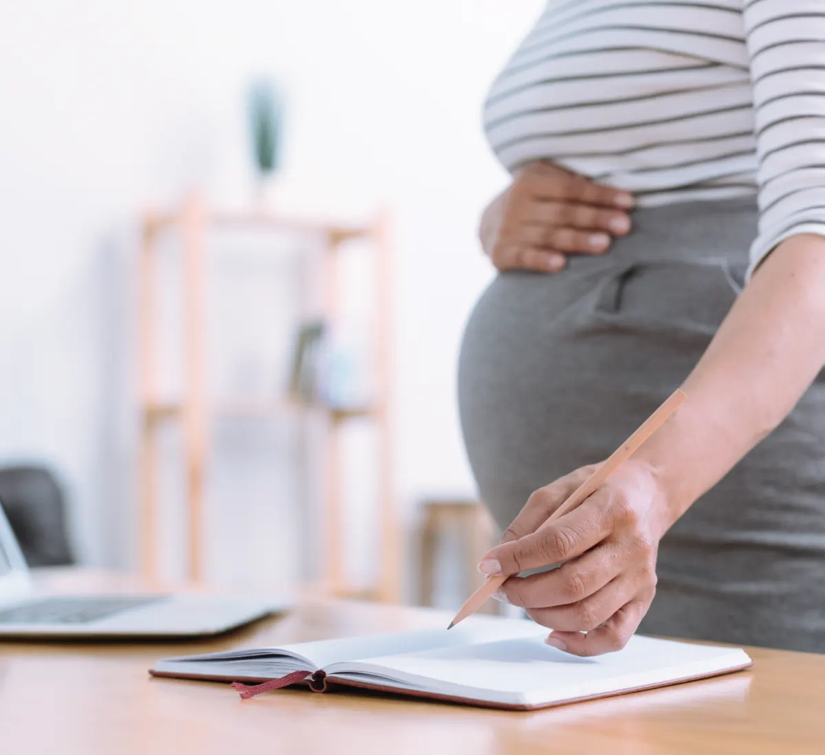 Pregnant woman writing in a notebook with one hand on her belly, symbolizing maternity rights and workplace protections.