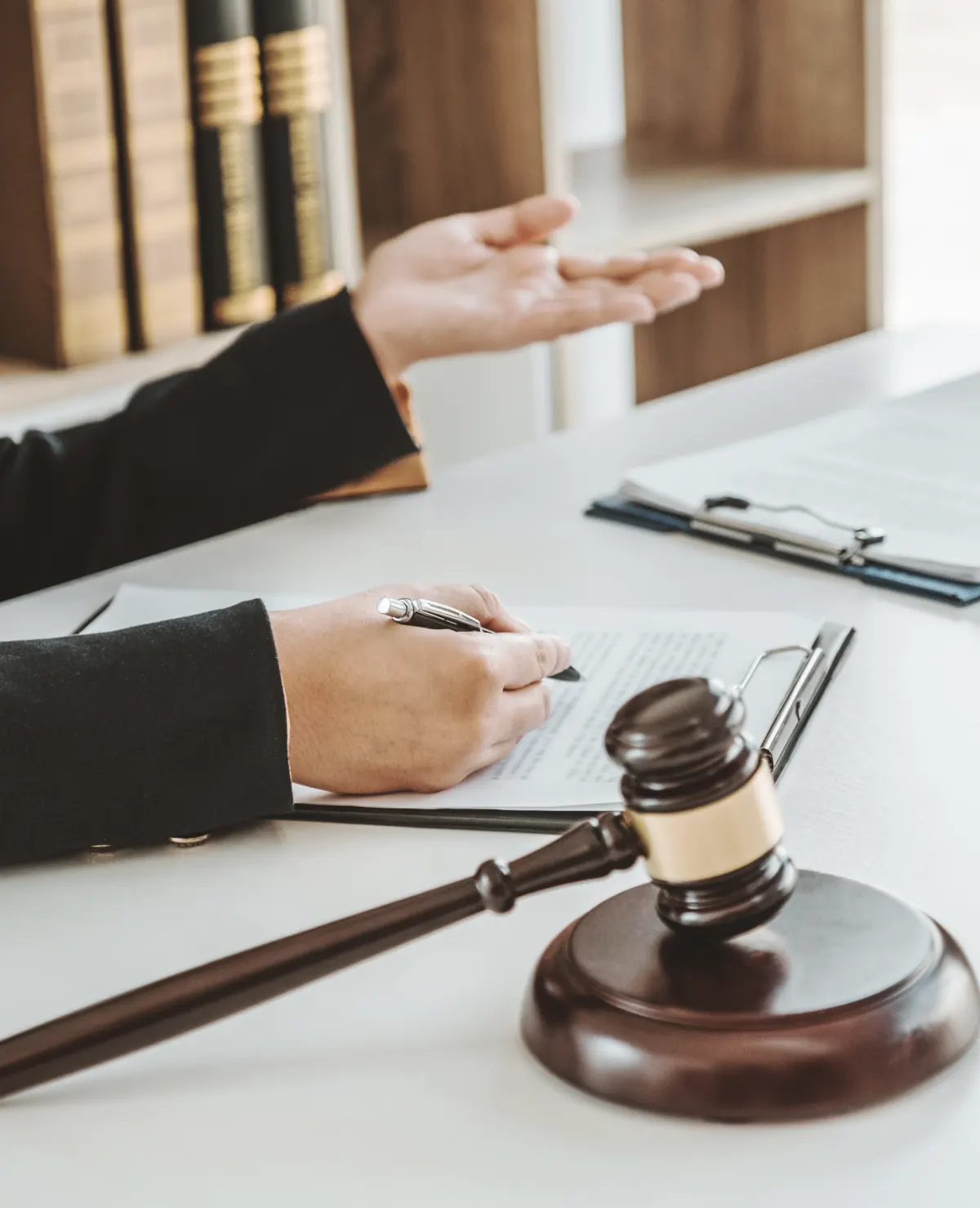 Close-up of a legal professional gesturing while reviewing documents with a gavel and clipboard on the desk, symbolizing legal consultation.