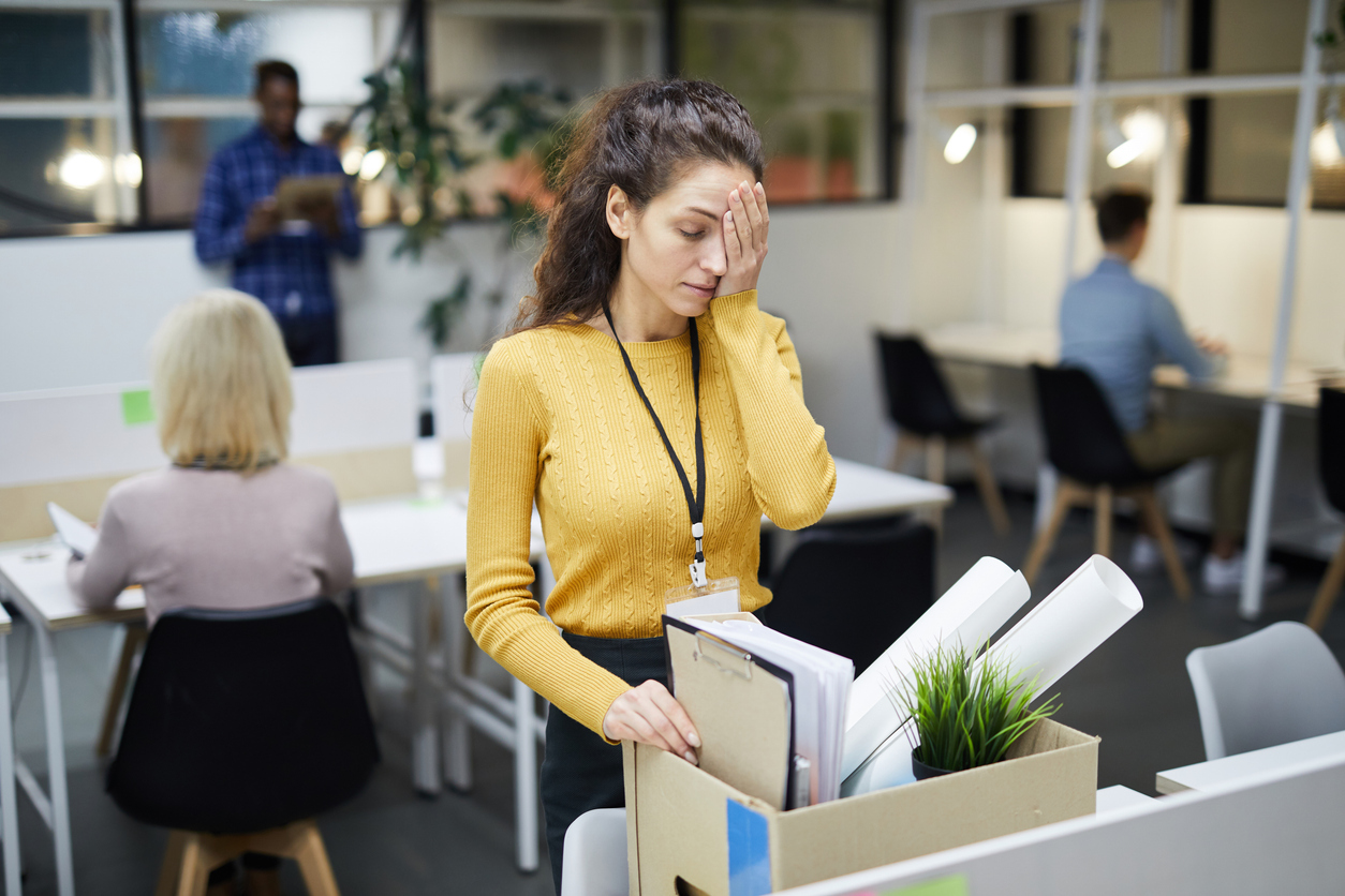 Upset woman carrying office supplies in a box after being terminated from her job, representing wrongful termination.