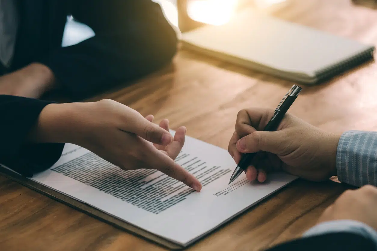 Close-up of a person signing a legal employment contract while another person explains details, symbolizing executive legal representation.