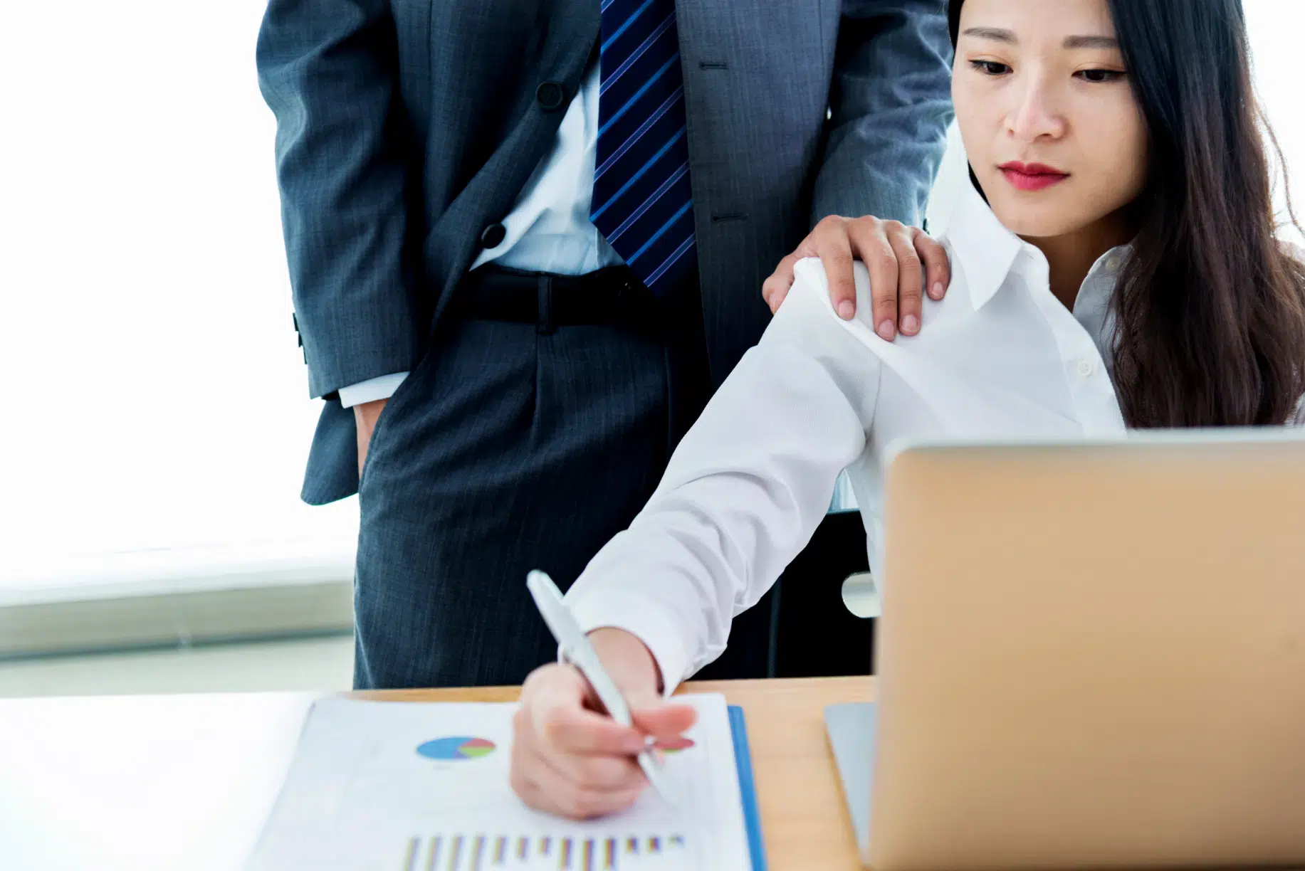 Man in a business suit placing a hand on a woman’s shoulder in an office setting, suggesting unwanted physical contact and a hostile work environment.